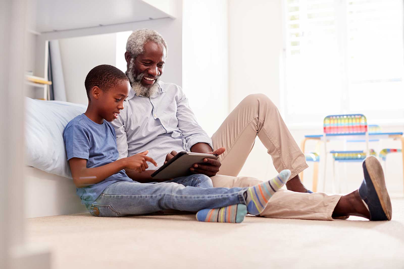 Foto de um avô com seu neto brincando em um tablet