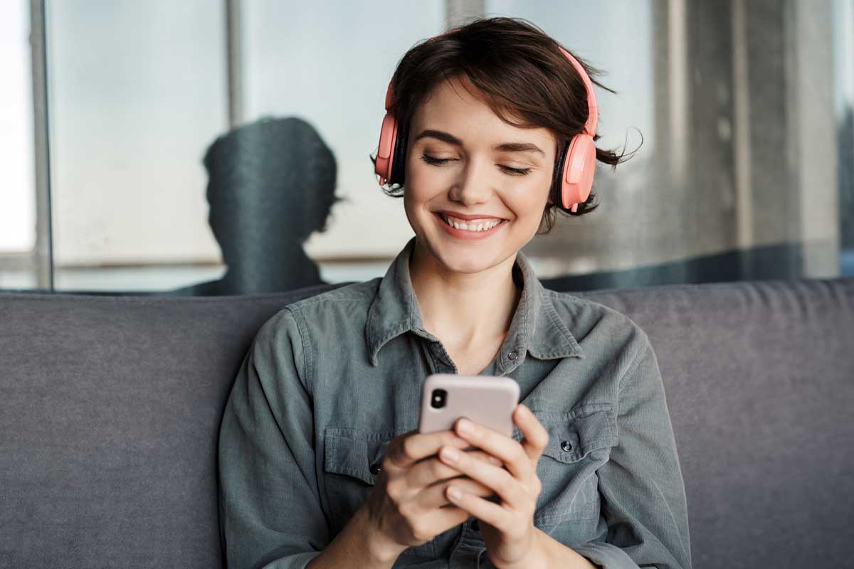 Uma pessoa usando fones de ouvido e escutando um áudio pelo smartphone.