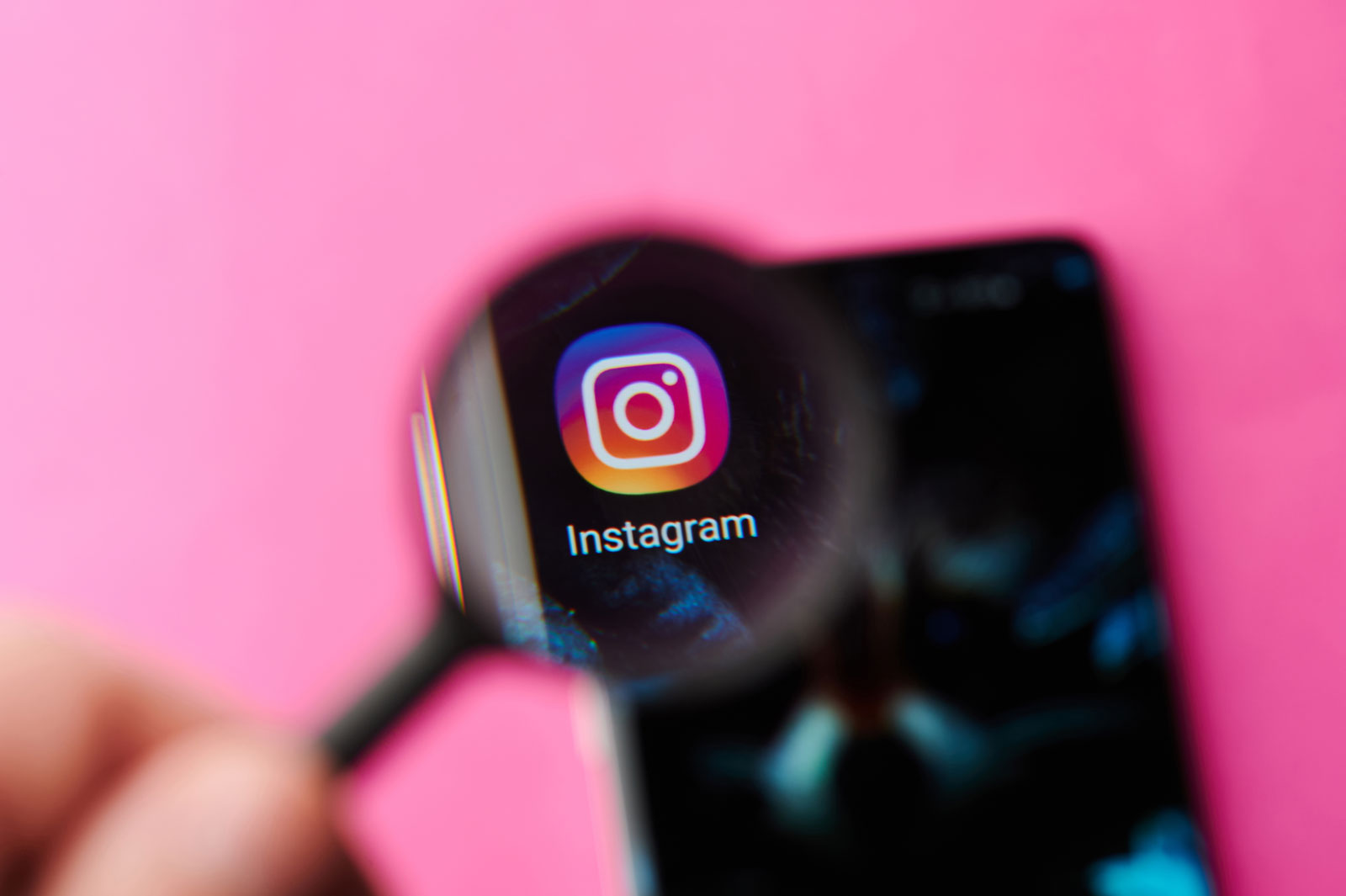 Uma pessoa segurando um lupa, que está aumentando o logo do Instagram em um smartphone